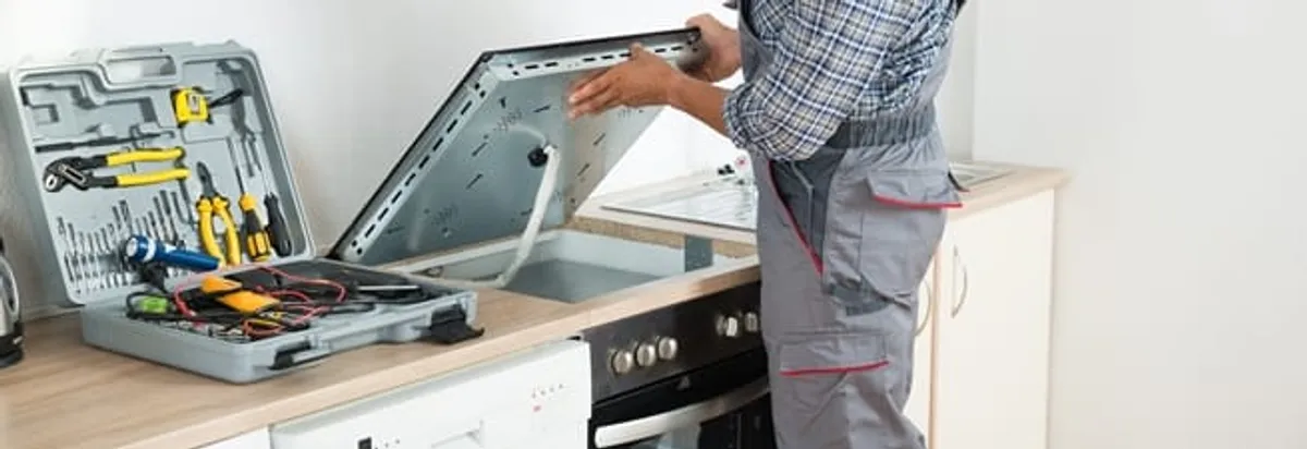 Cooktop repair technician lifting a built-in stovetop for service in Tacoma, WA